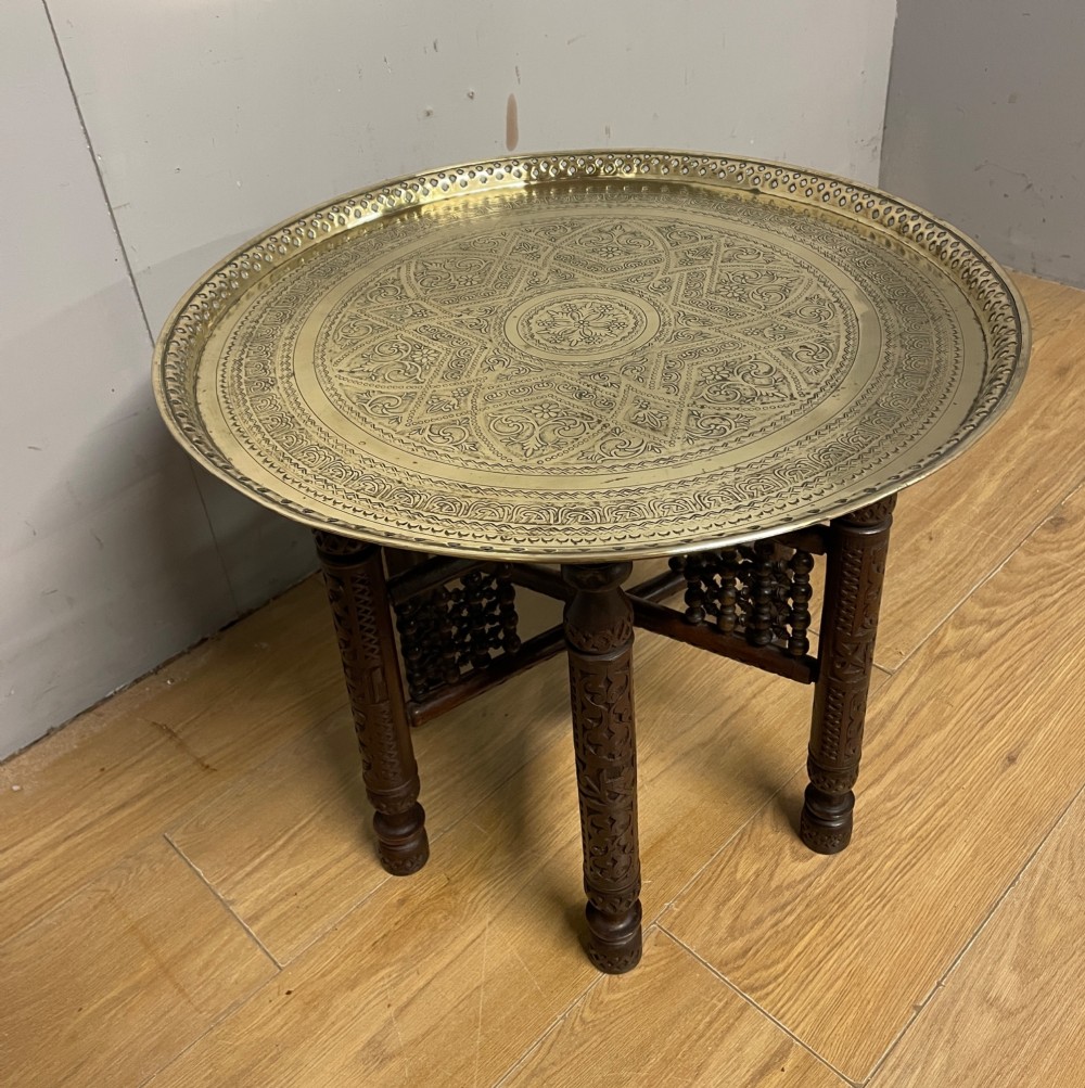 A late 19th-century Anglo-Indian Benares table featuring an intricately engraved circular brass tray top resting on a dark carved wooden folding base. View V