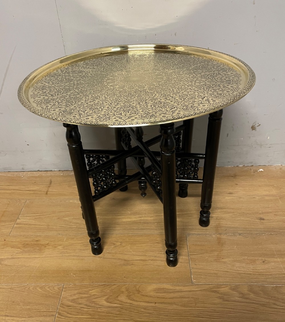 An Anglo-Indian circular brass tray table with hand-engraved patterns supported on an ebonised wooden base with turned legs.