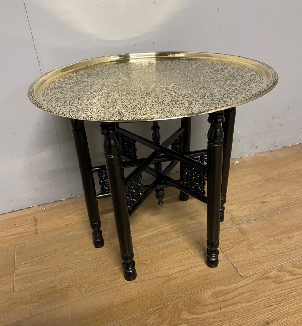 An Anglo-Indian circular brass tray table with hand-engraved patterns supported on an ebonised wooden base with turned legs. View II