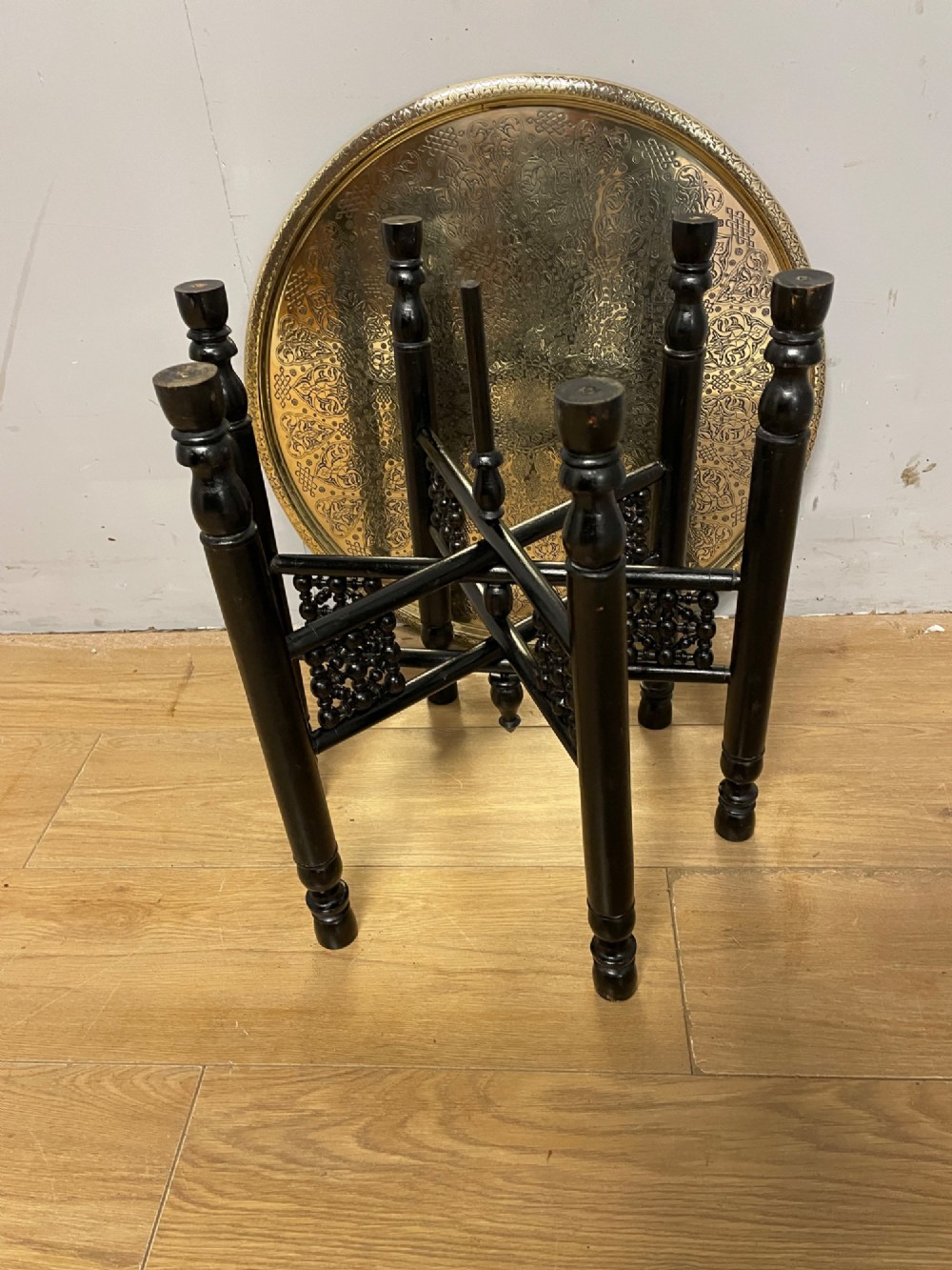 An Anglo-Indian circular brass tray table with hand-engraved patterns supported on an ebonised wooden base with turned legs. View VI