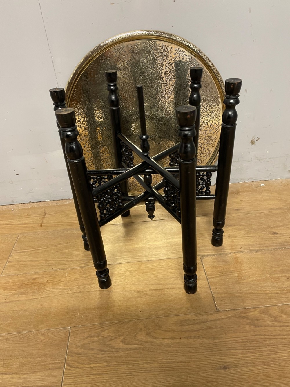 An Anglo-Indian circular brass tray table with hand-engraved patterns supported on an ebonised wooden base with turned legs. View VII