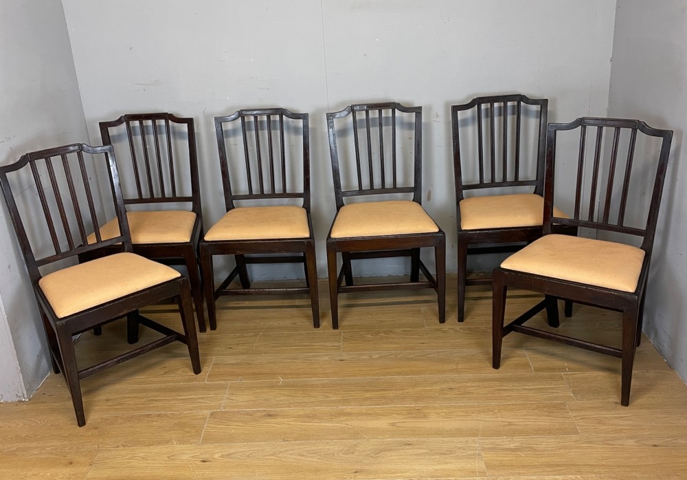 A set of six late Georgian dark mahogany country-made dining chairs featuring vertical bar backs and padded light tan upholstered drop-in seats.