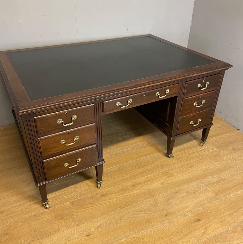 An Edwardian mahogany partners desk featuring a green leather writing surface, brass swan-neck handles, fluted pilasters, and tapered legs on castors. View II