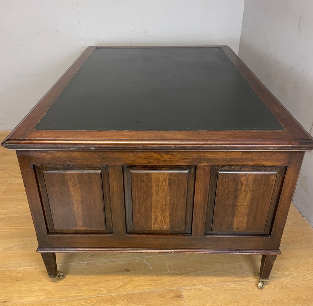 An Edwardian mahogany partners desk featuring a green leather writing surface, brass swan-neck handles, fluted pilasters, and tapered legs on castors. View VII