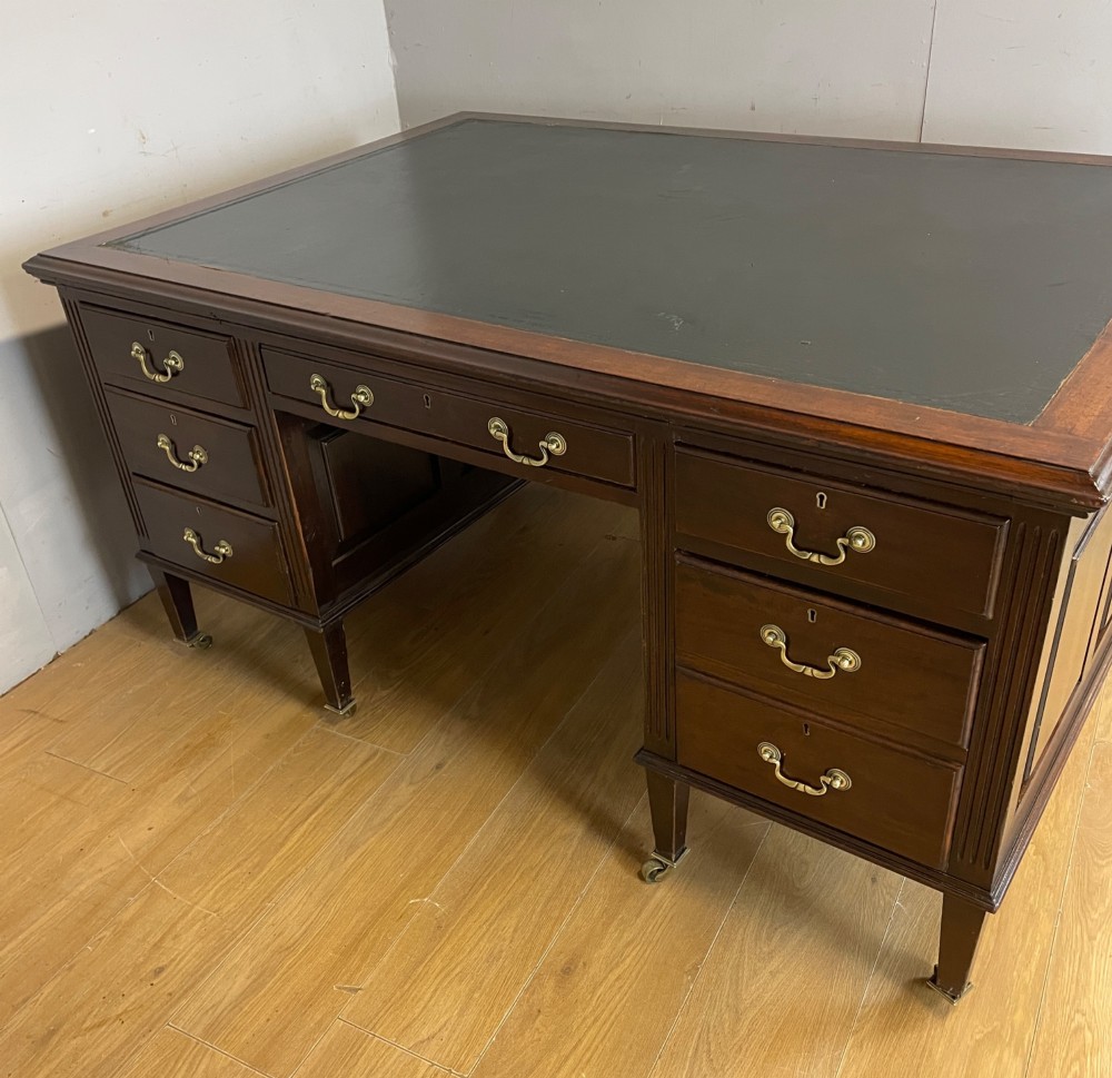 An Edwardian mahogany partners desk featuring a green leather writing surface, brass swan-neck handles, fluted pilasters, and tapered legs on castors. View VIII