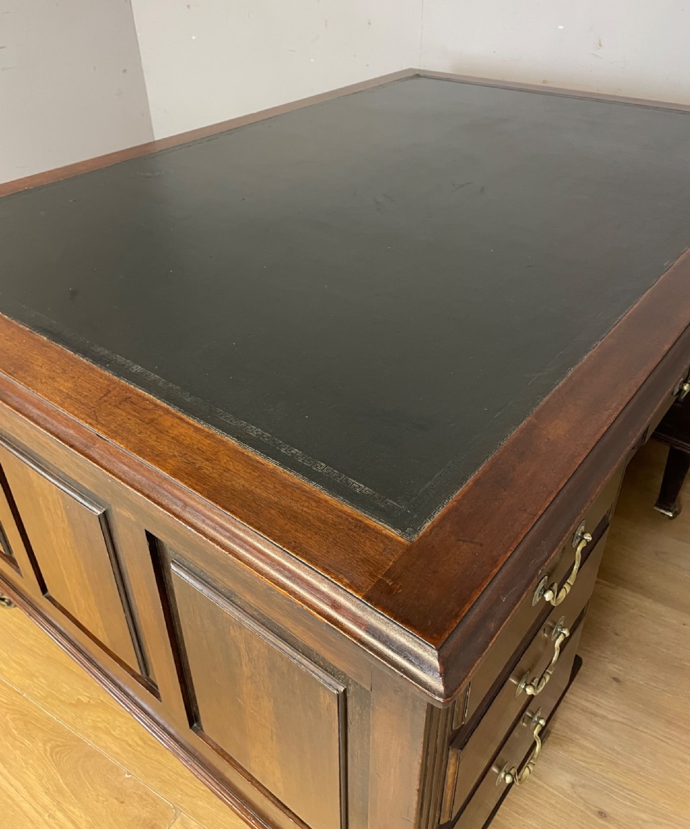 An Edwardian mahogany partners desk featuring a green leather writing surface, brass swan-neck handles, fluted pilasters, and tapered legs on castors. View X