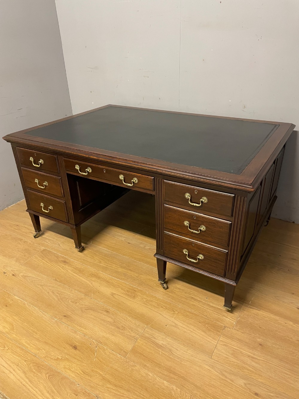 An Edwardian mahogany partners desk featuring a green leather writing surface, brass swan-neck handles, fluted pilasters, and tapered legs on castors. View XII