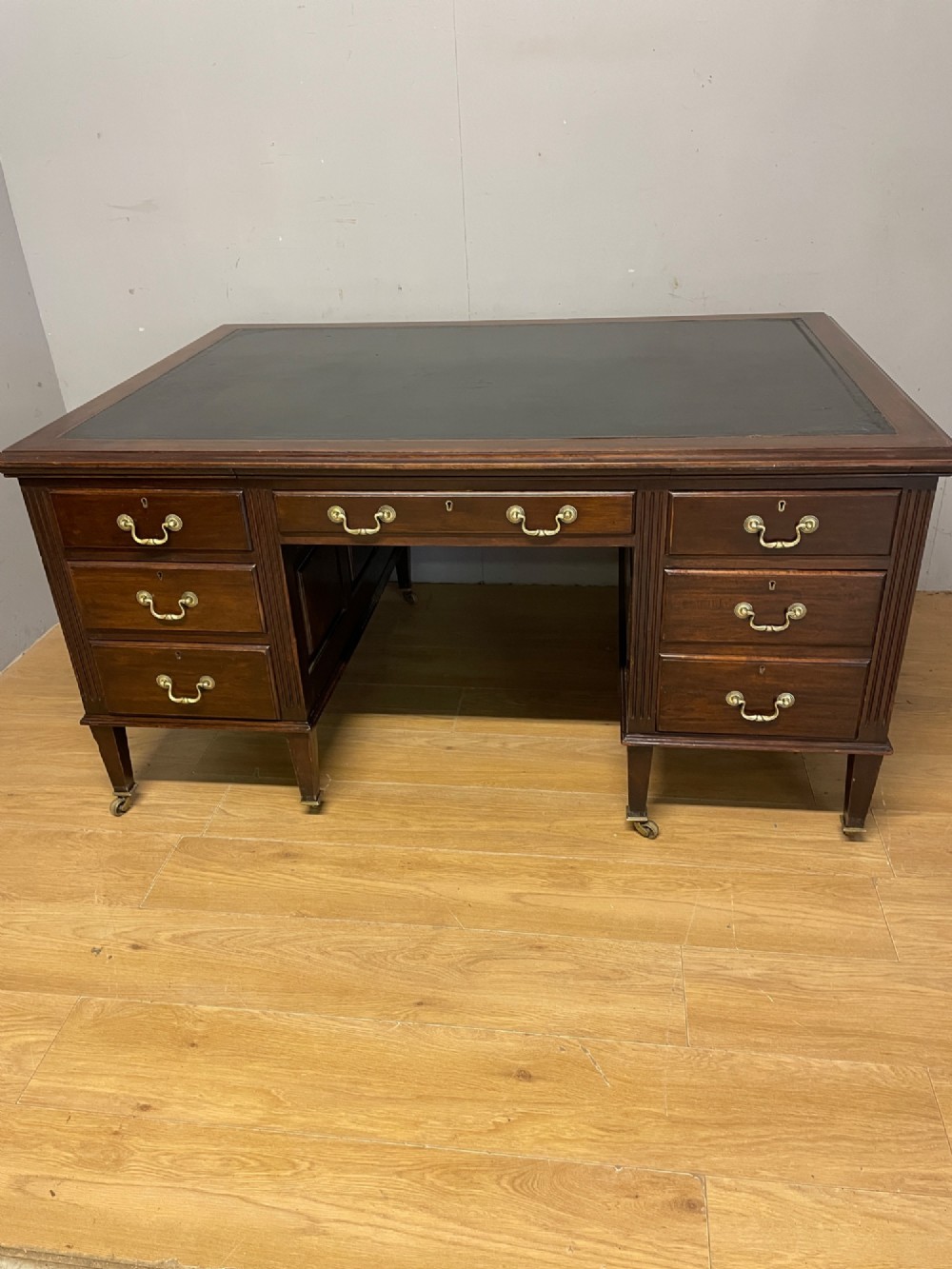 An Edwardian mahogany partners desk featuring a green leather writing surface, brass swan-neck handles, fluted pilasters, and tapered legs on castors. View XIII