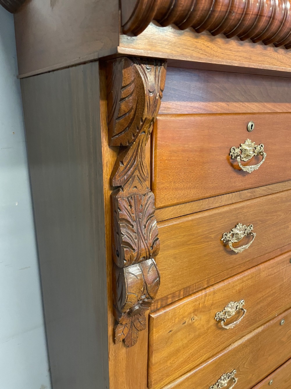 A 19th-century Scottish walnut chest of drawers featuring carved acanthus corbels, a gadrooned top frieze, and ornate brass drop handles. View VI