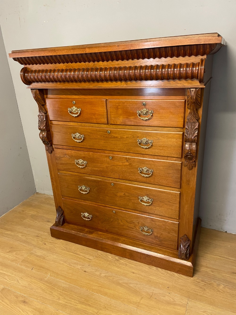 A 19th-century Scottish walnut chest of drawers featuring carved acanthus corbels, a gadrooned top frieze, and ornate brass drop handles. View X