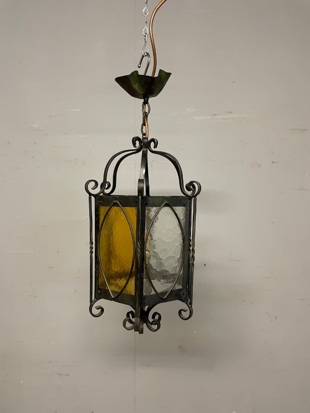 An illuminated hexagonal wrought iron hall lantern with textured amber glass panels and decorative scrollwork. View V