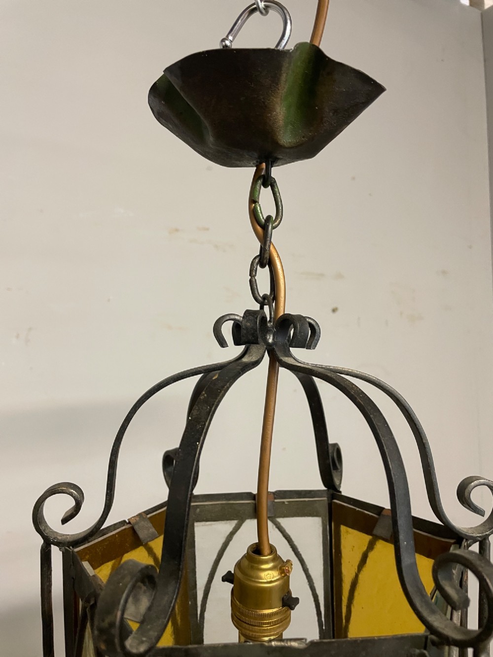 An illuminated hexagonal wrought iron hall lantern with textured amber glass panels and decorative scrollwork. View VI