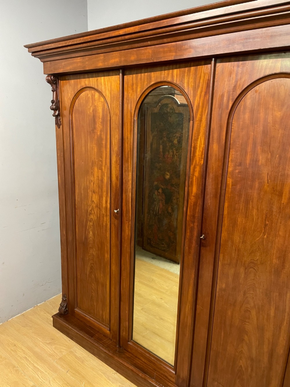 A 19th-century flame mahogany triple wardrobe with an arched central mirrored door flanked by two panelled doors, topped with a stepped cornice and carved corbels. View III