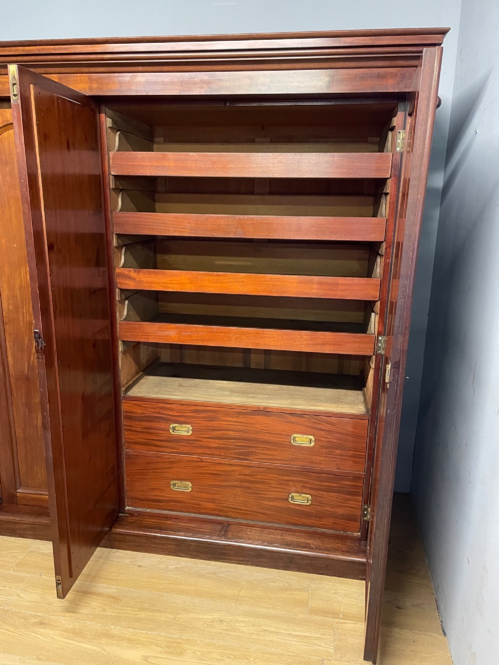 A 19th-century flame mahogany triple wardrobe with an arched central mirrored door flanked by two panelled doors, topped with a stepped cornice and carved corbels. View V