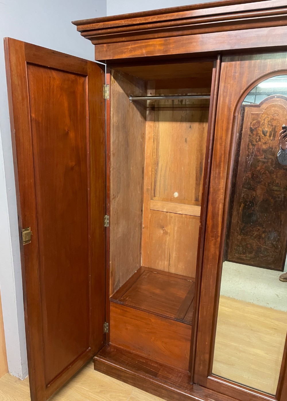 A 19th-century flame mahogany triple wardrobe with an arched central mirrored door flanked by two panelled doors, topped with a stepped cornice and carved corbels. View VI