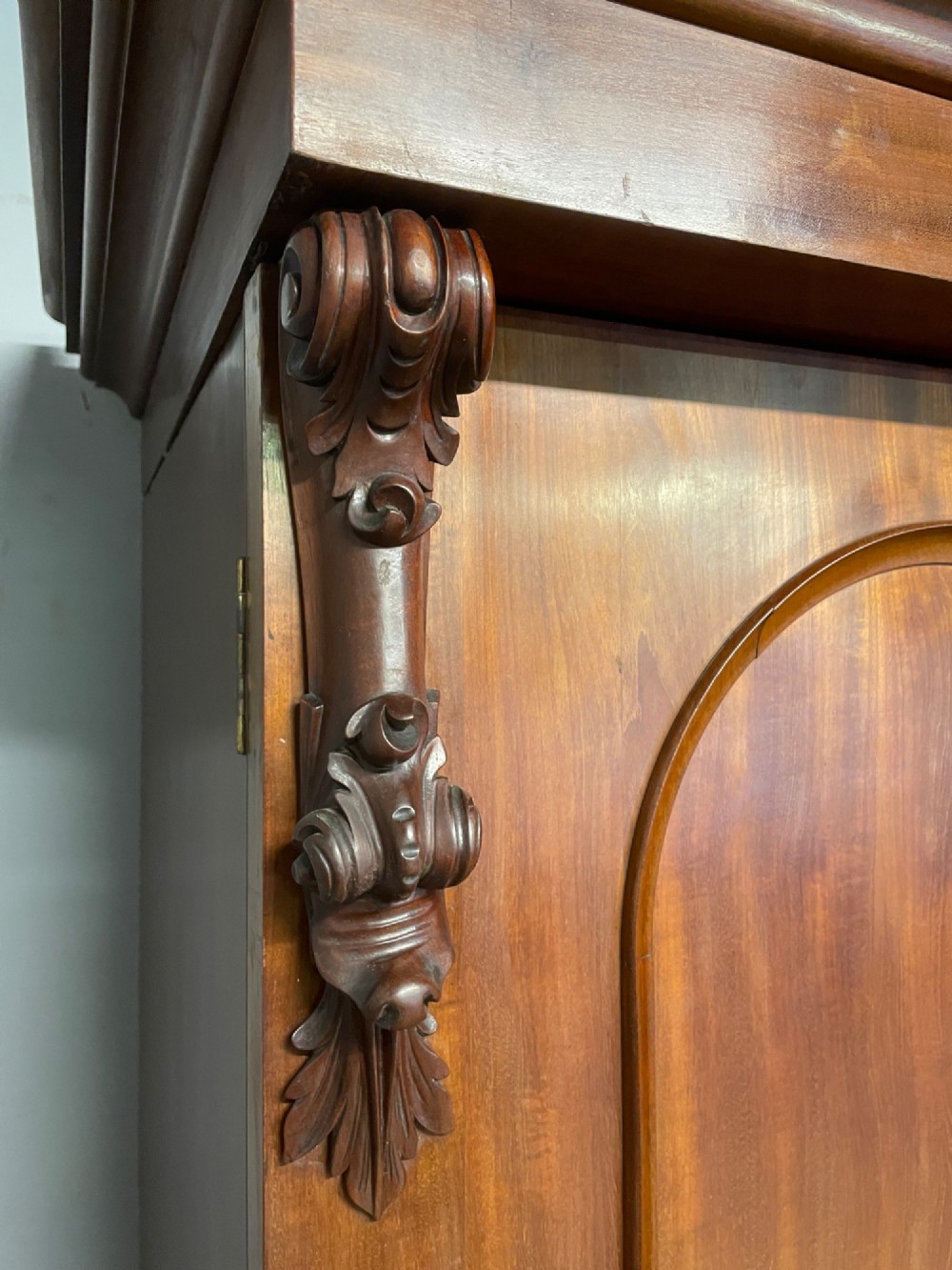 A 19th-century flame mahogany triple wardrobe with an arched central mirrored door flanked by two panelled doors, topped with a stepped cornice and carved corbels. View VII