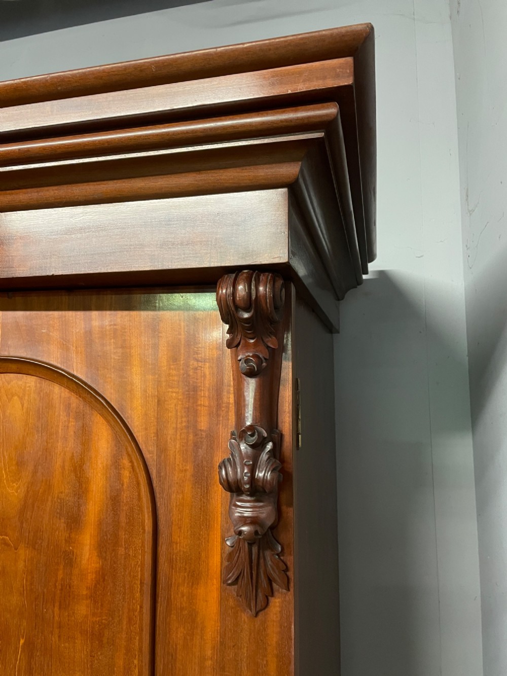 A 19th-century flame mahogany triple wardrobe with an arched central mirrored door flanked by two panelled doors, topped with a stepped cornice and carved corbels. View IX