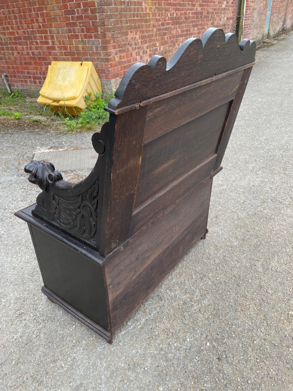 A 19th-century dark oak box settle with carved floral panels, lion mask terminals, a decorative cresting rail, and a lift-up storage seat. View VIII