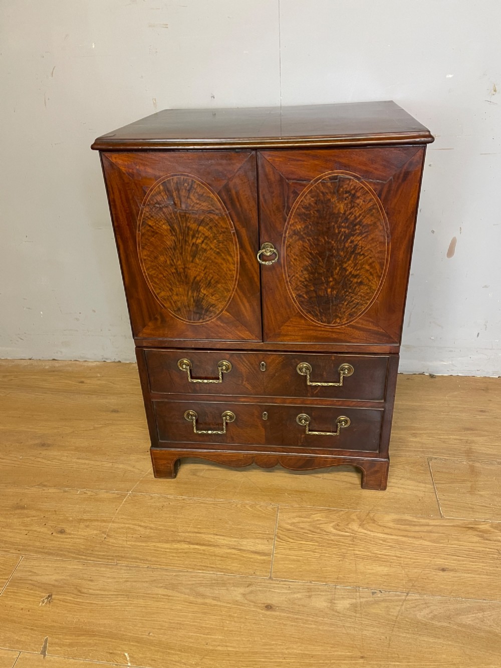 A Georgian mahogany side cabinet featuring oval flame veneer inlaid cupboard doors above two drawers with brass handles, resting on bracket feet. View II