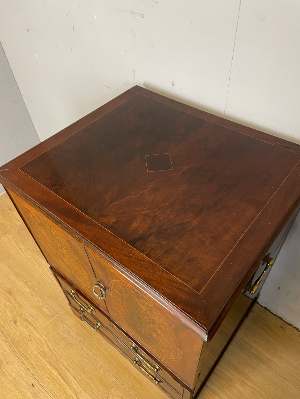 A Georgian mahogany side cabinet featuring oval flame veneer inlaid cupboard doors above two drawers with brass handles, resting on bracket feet. View IV