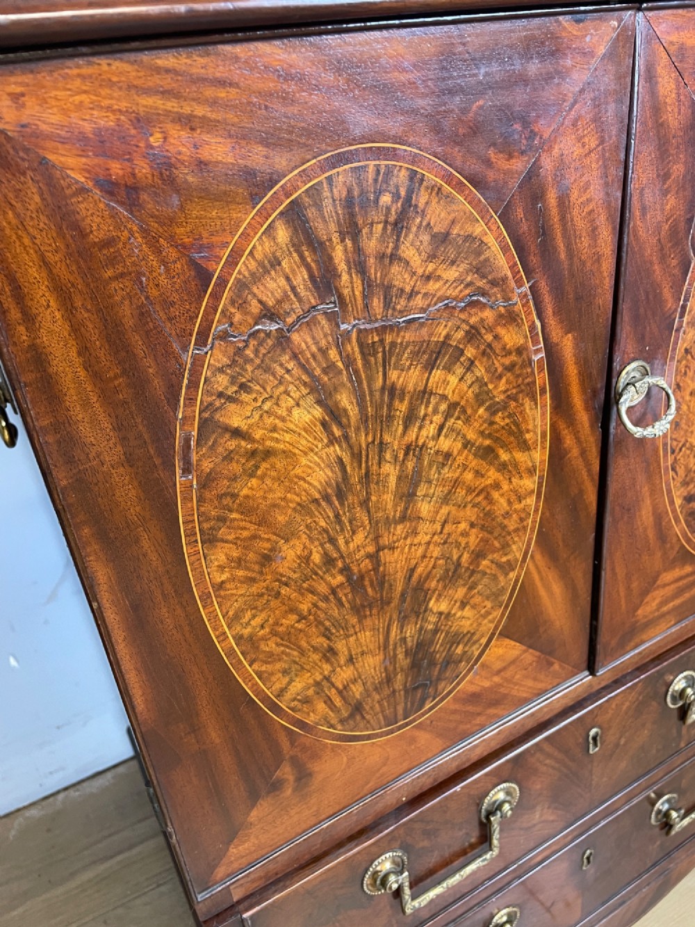 A Georgian mahogany side cabinet featuring oval flame veneer inlaid cupboard doors above two drawers with brass handles, resting on bracket feet. View VI