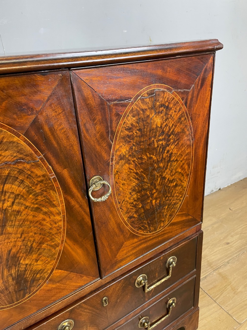 A Georgian mahogany side cabinet featuring oval flame veneer inlaid cupboard doors above two drawers with brass handles, resting on bracket feet. View VII