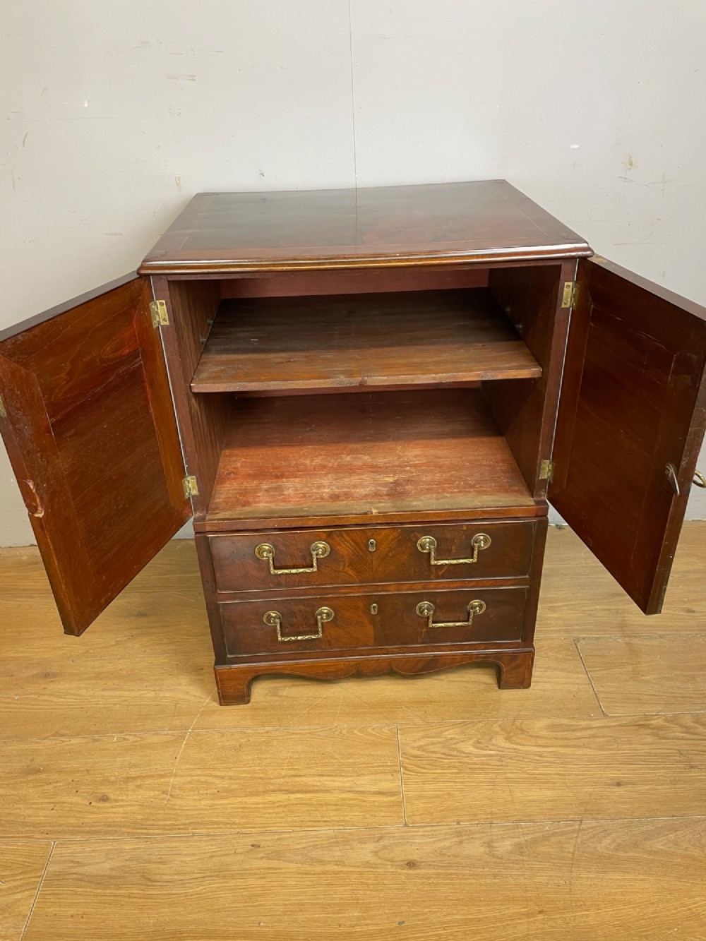 A Georgian mahogany side cabinet featuring oval flame veneer inlaid cupboard doors above two drawers with brass handles, resting on bracket feet. View VIII