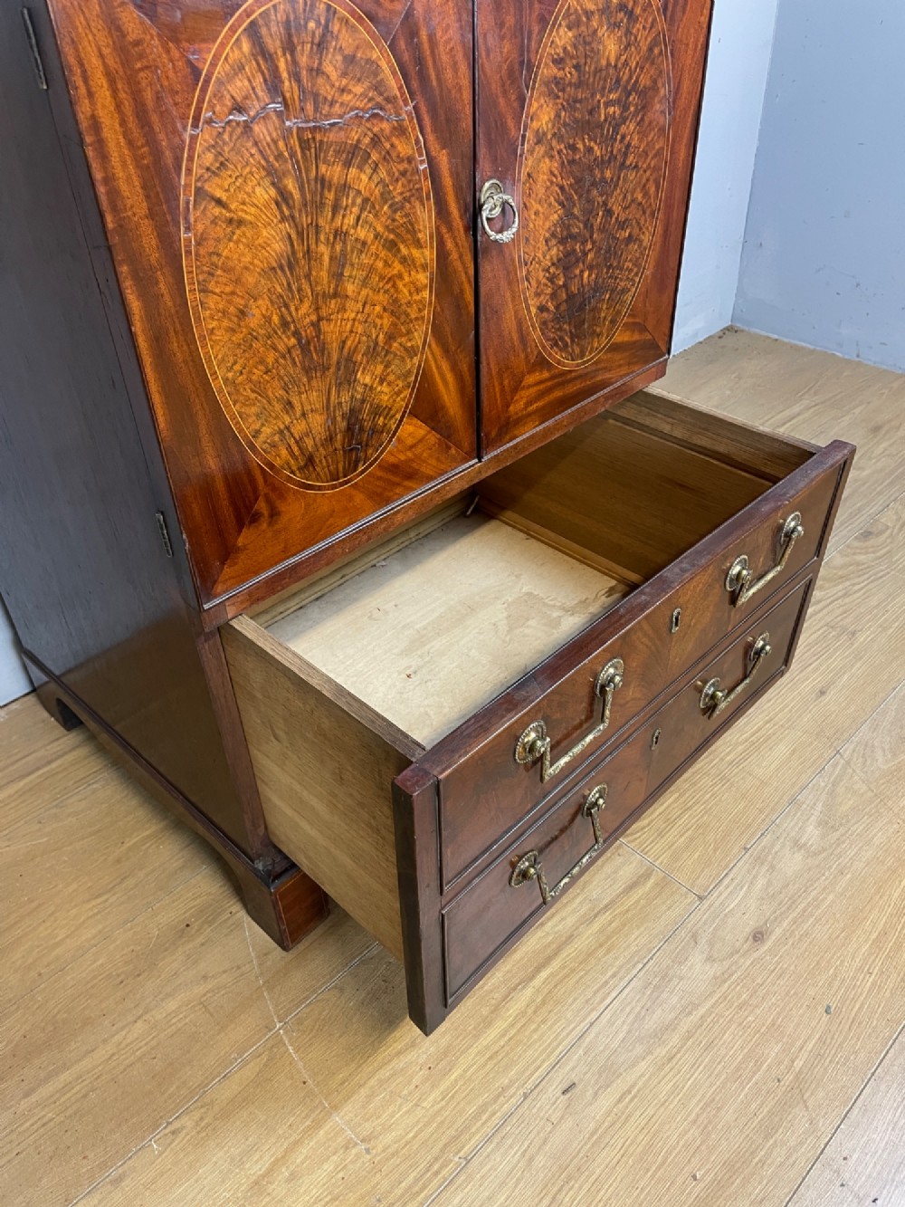 A Georgian mahogany side cabinet featuring oval flame veneer inlaid cupboard doors above two drawers with brass handles, resting on bracket feet. View IX