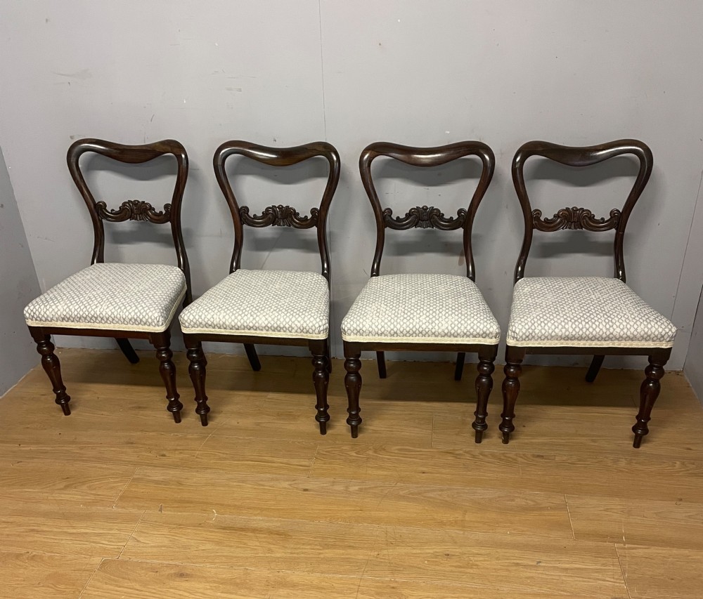 A set of four Victorian rosewood balloon back dining chairs with carved mid-rails, turned front legs, and grey patterned upholstered seats.