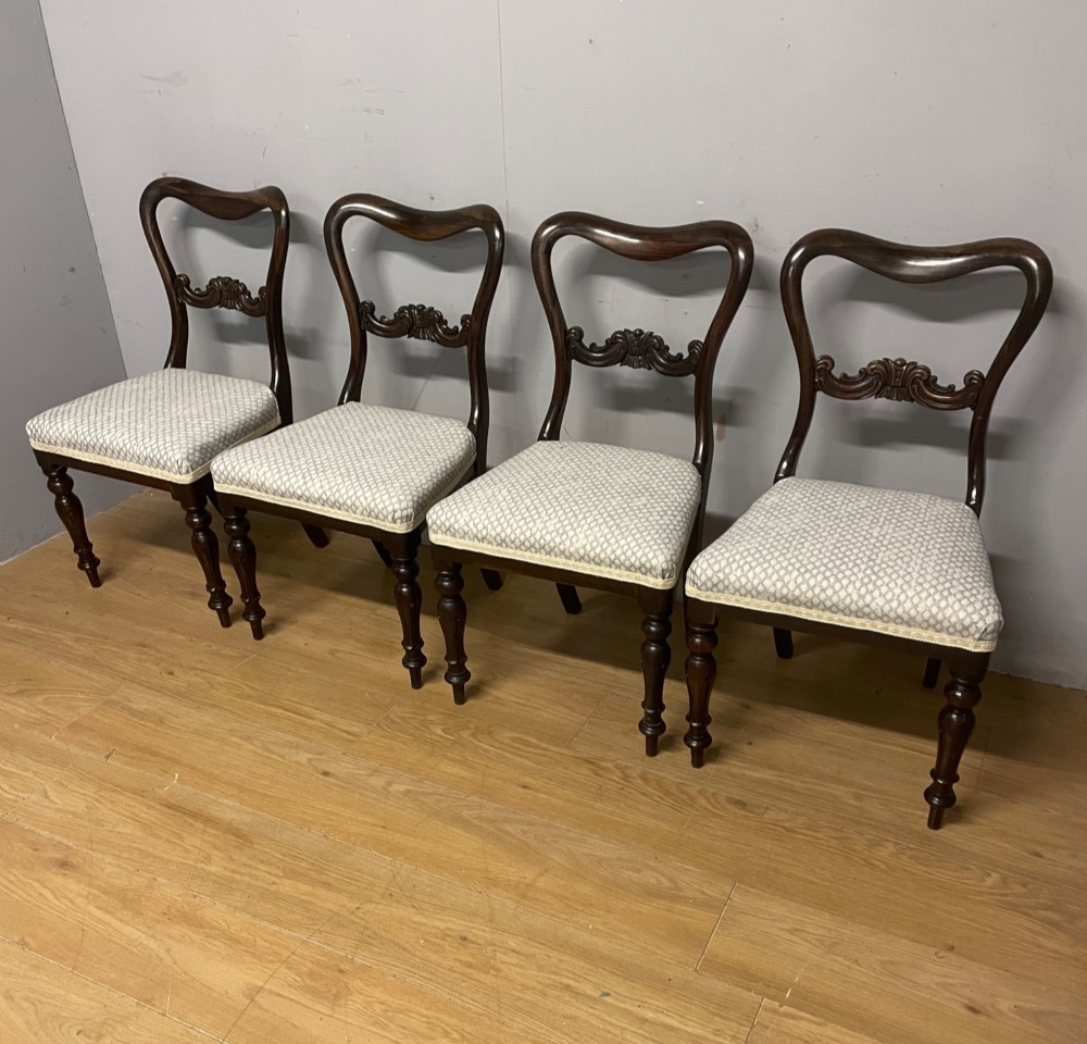 A set of four Victorian rosewood balloon back dining chairs with carved mid-rails, turned front legs, and grey patterned upholstered seats. View II