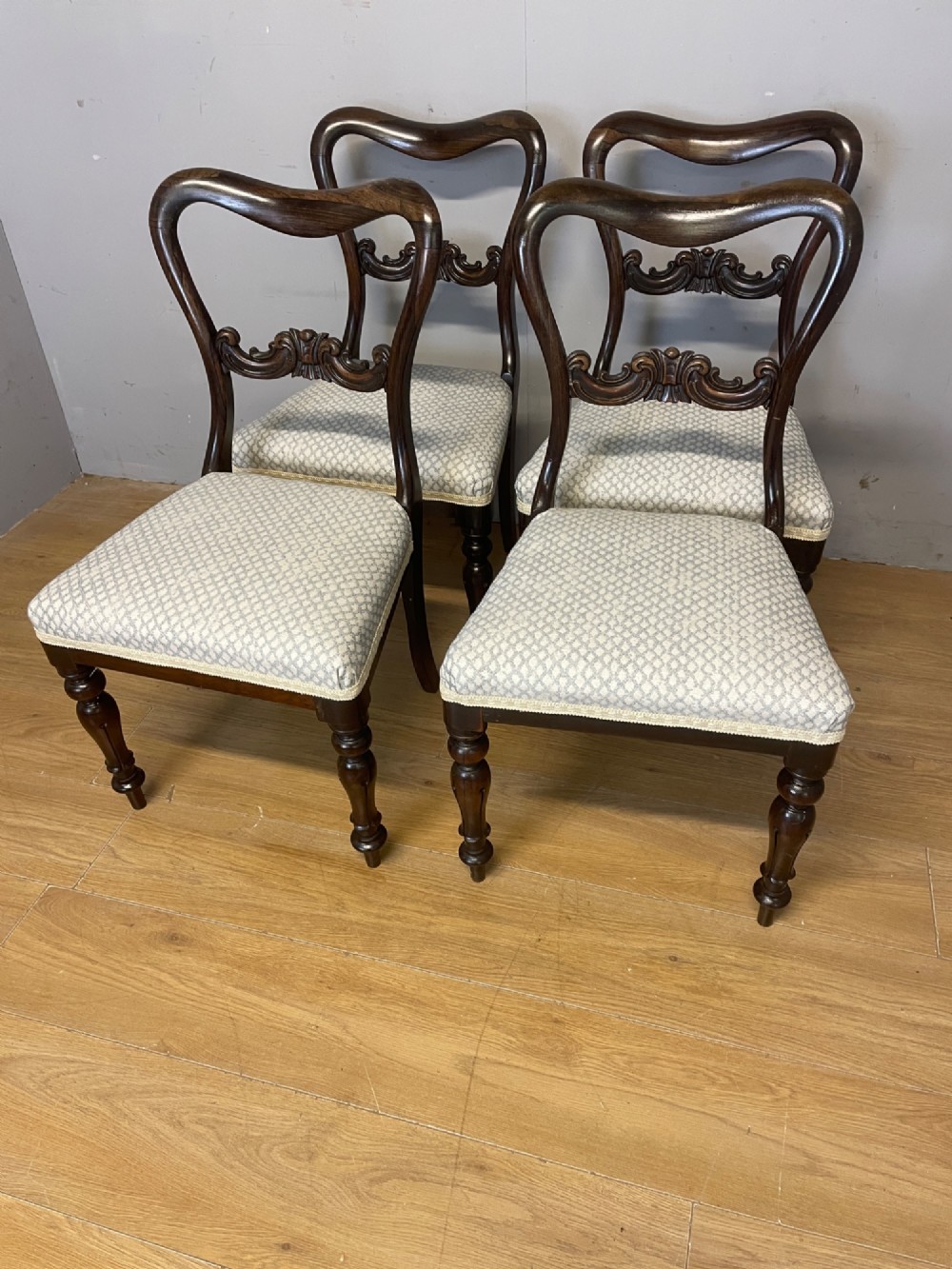 A set of four Victorian rosewood balloon back dining chairs with carved mid-rails, turned front legs, and grey patterned upholstered seats. View VI