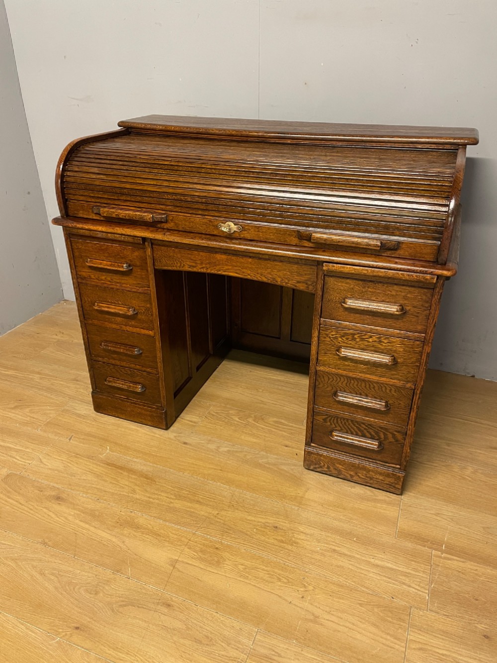 An Edwardian solid oak twin-pedestal roll top desk featuring a curved tambour front, fitted drawers with integrated wooden handles, and a central brass keyhole.