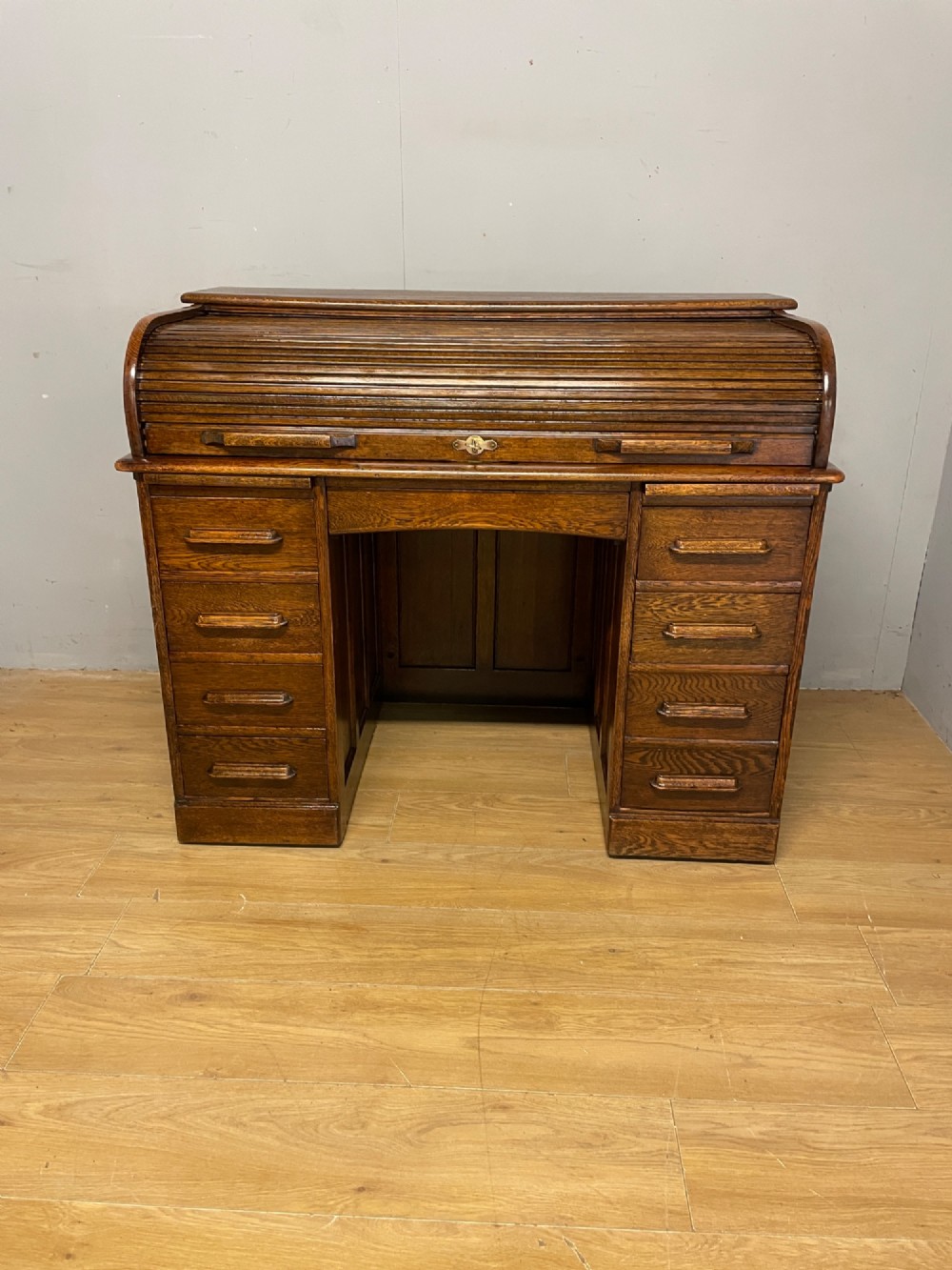 An Edwardian solid oak twin-pedestal roll top desk featuring a curved tambour front, fitted drawers with integrated wooden handles, and a central brass keyhole. View II