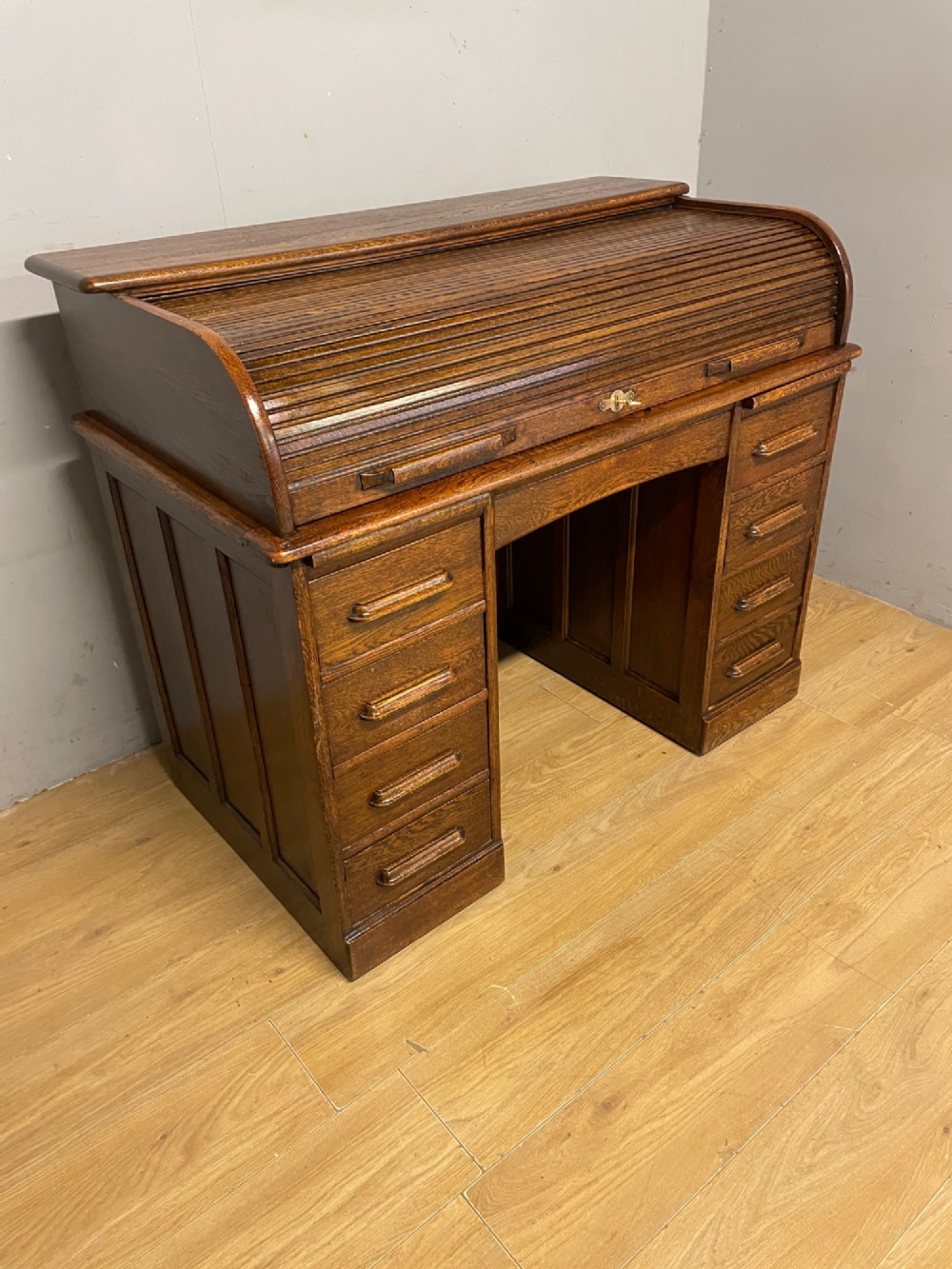 An Edwardian solid oak twin-pedestal roll top desk featuring a curved tambour front, fitted drawers with integrated wooden handles, and a central brass keyhole. View III