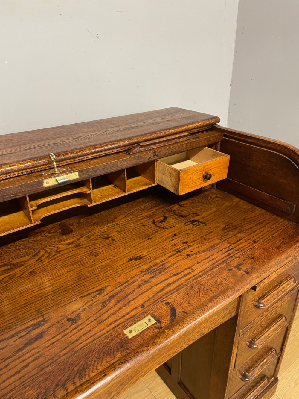 An Edwardian solid oak twin-pedestal roll top desk featuring a curved tambour front, fitted drawers with integrated wooden handles, and a central brass keyhole. View VI