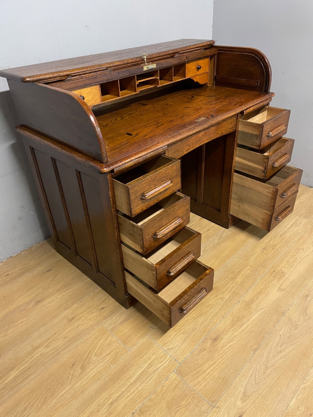 An Edwardian solid oak twin-pedestal roll top desk featuring a curved tambour front, fitted drawers with integrated wooden handles, and a central brass keyhole. View VIII
