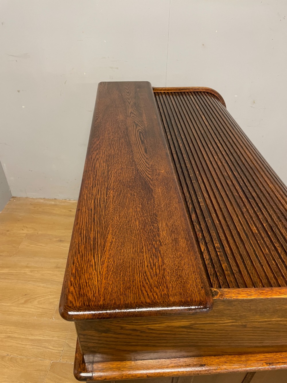 An Edwardian solid oak twin-pedestal roll top desk featuring a curved tambour front, fitted drawers with integrated wooden handles, and a central brass keyhole. View XI