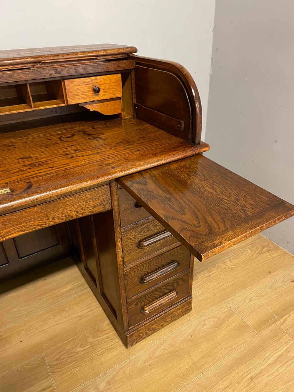 An Edwardian solid oak twin-pedestal roll top desk featuring a curved tambour front, fitted drawers with integrated wooden handles, and a central brass keyhole. View XII