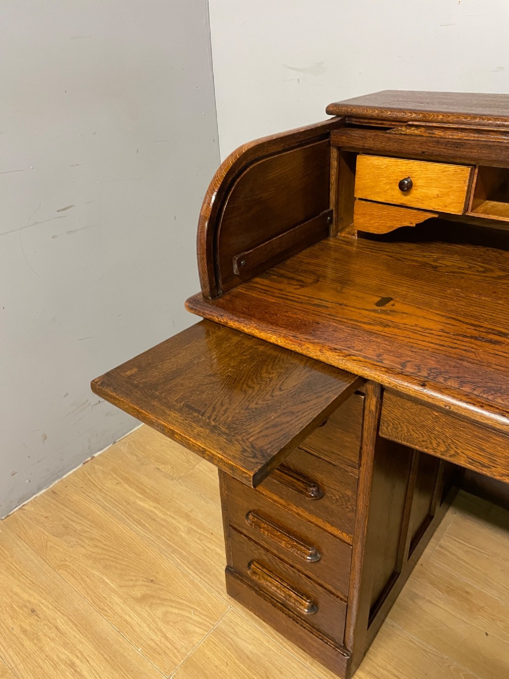 An Edwardian solid oak twin-pedestal roll top desk featuring a curved tambour front, fitted drawers with integrated wooden handles, and a central brass keyhole. View XIII