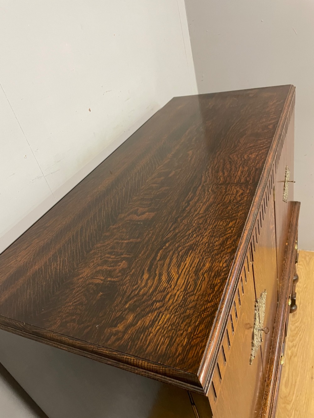 A solid dark oak Jacobean style side cabinet featuring brass escutcheons, carved moulding along the top edge, two lower drawers, and turned legs connected by a lower stretcher. View V