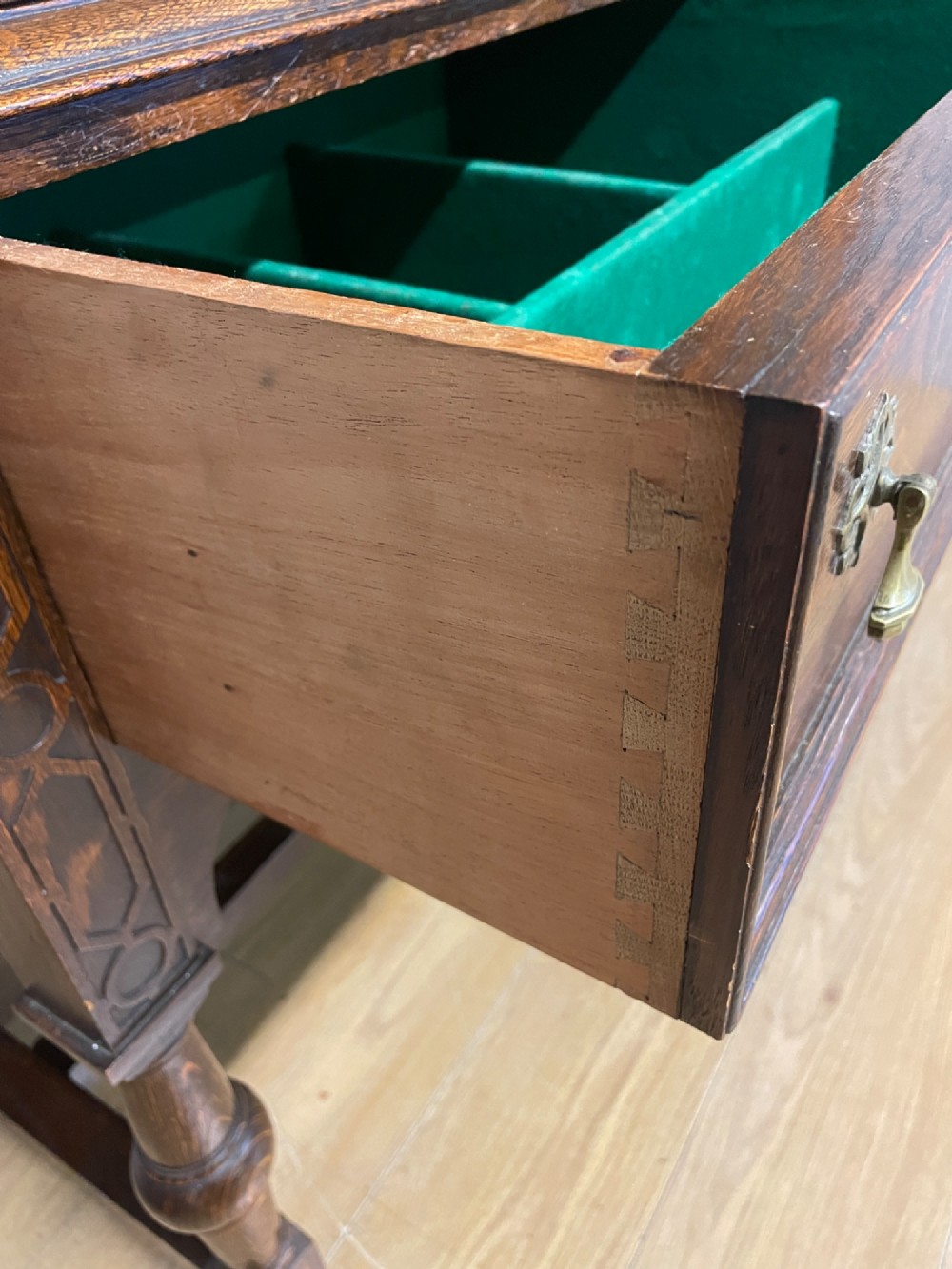A solid dark oak Jacobean style side cabinet featuring brass escutcheons, carved moulding along the top edge, two lower drawers, and turned legs connected by a lower stretcher. View VIII