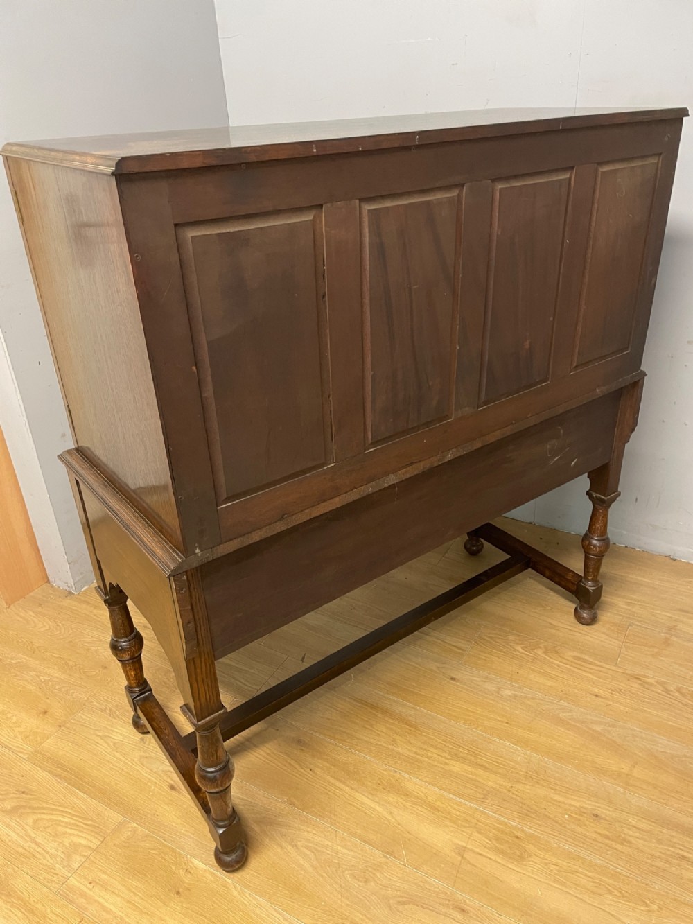 A solid dark oak Jacobean style side cabinet featuring brass escutcheons, carved moulding along the top edge, two lower drawers, and turned legs connected by a lower stretcher. View XI