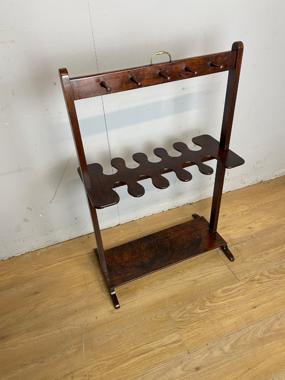 A dark mahogany Georgian boot and whip rack featuring an upper row of turned pegs, a brass handle, a central cutout shelf, and a solid base.