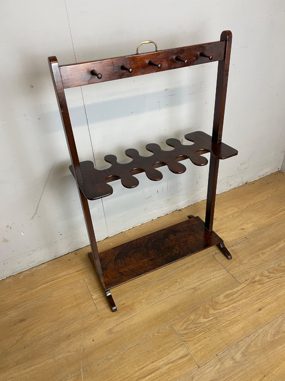 A dark mahogany Georgian boot and whip rack featuring an upper row of turned pegs, a brass handle, a central cutout shelf, and a solid base. View II