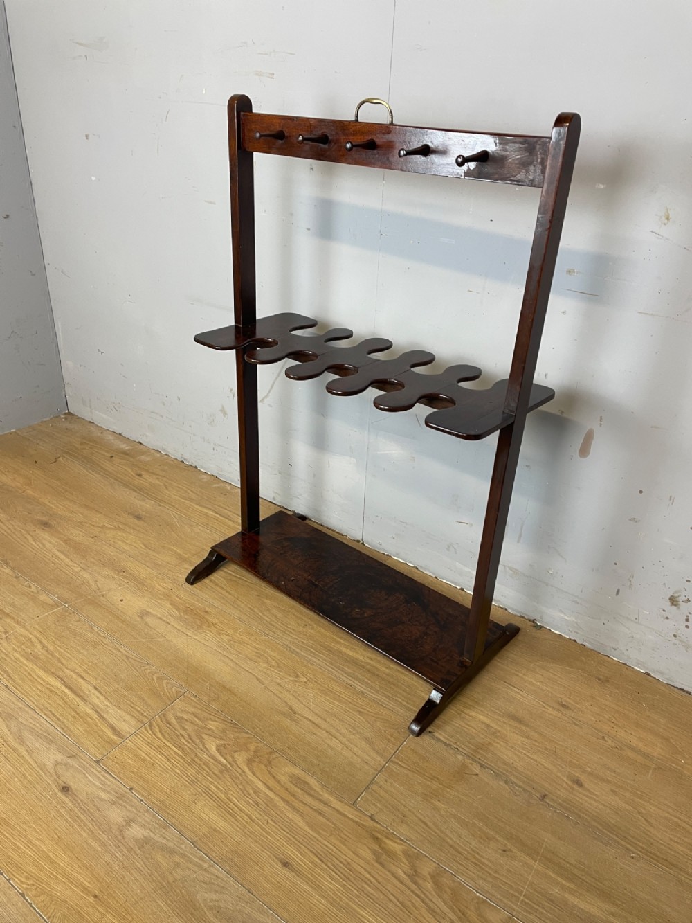 A dark mahogany Georgian boot and whip rack featuring an upper row of turned pegs, a brass handle, a central cutout shelf, and a solid base. View III