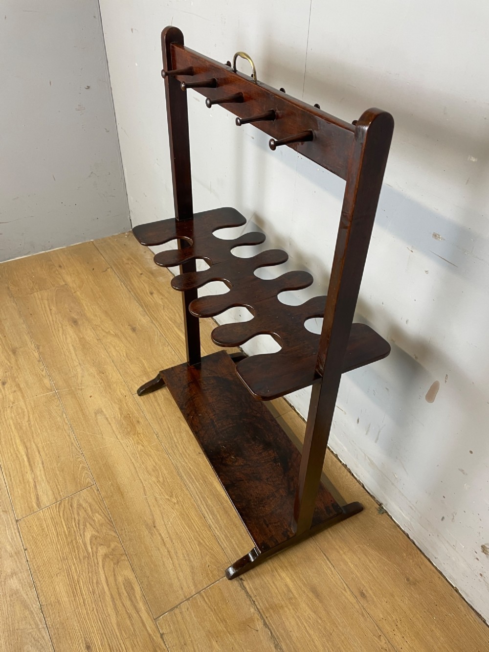 A dark mahogany Georgian boot and whip rack featuring an upper row of turned pegs, a brass handle, a central cutout shelf, and a solid base. View IV