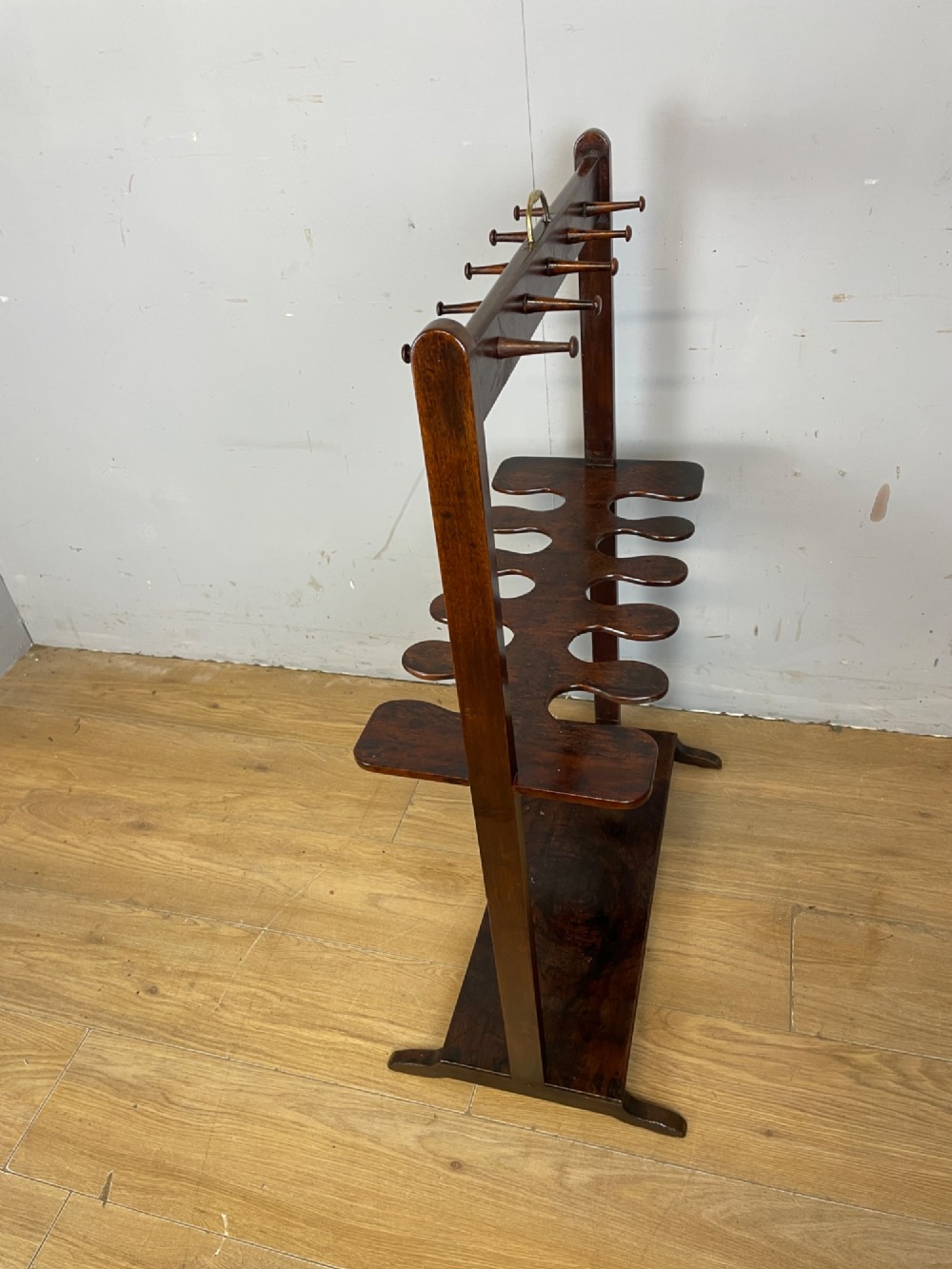 A dark mahogany Georgian boot and whip rack featuring an upper row of turned pegs, a brass handle, a central cutout shelf, and a solid base. View V