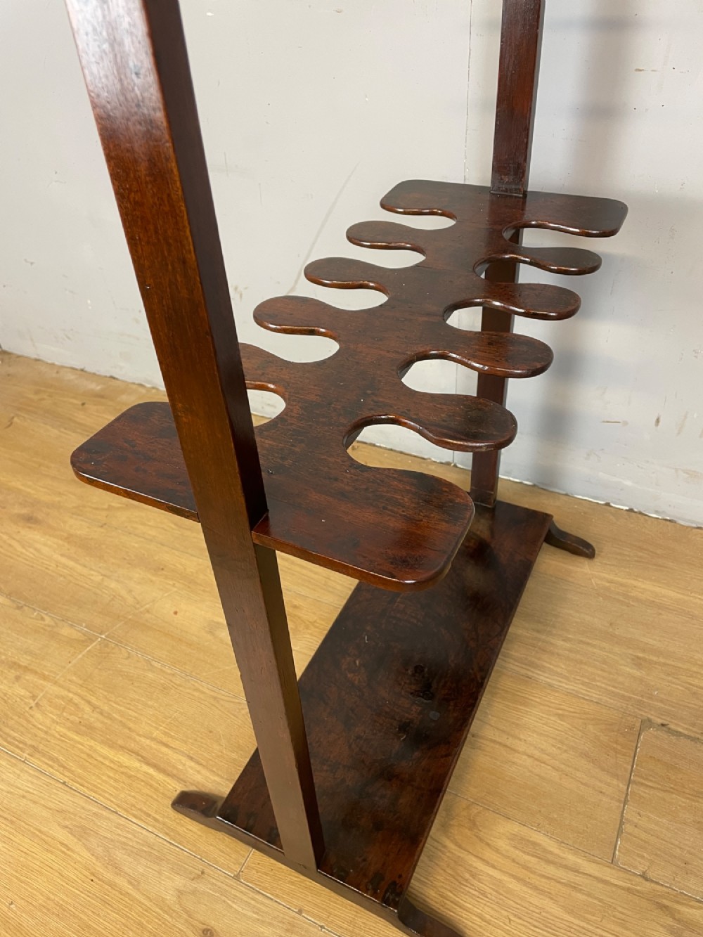A dark mahogany Georgian boot and whip rack featuring an upper row of turned pegs, a brass handle, a central cutout shelf, and a solid base. View VI