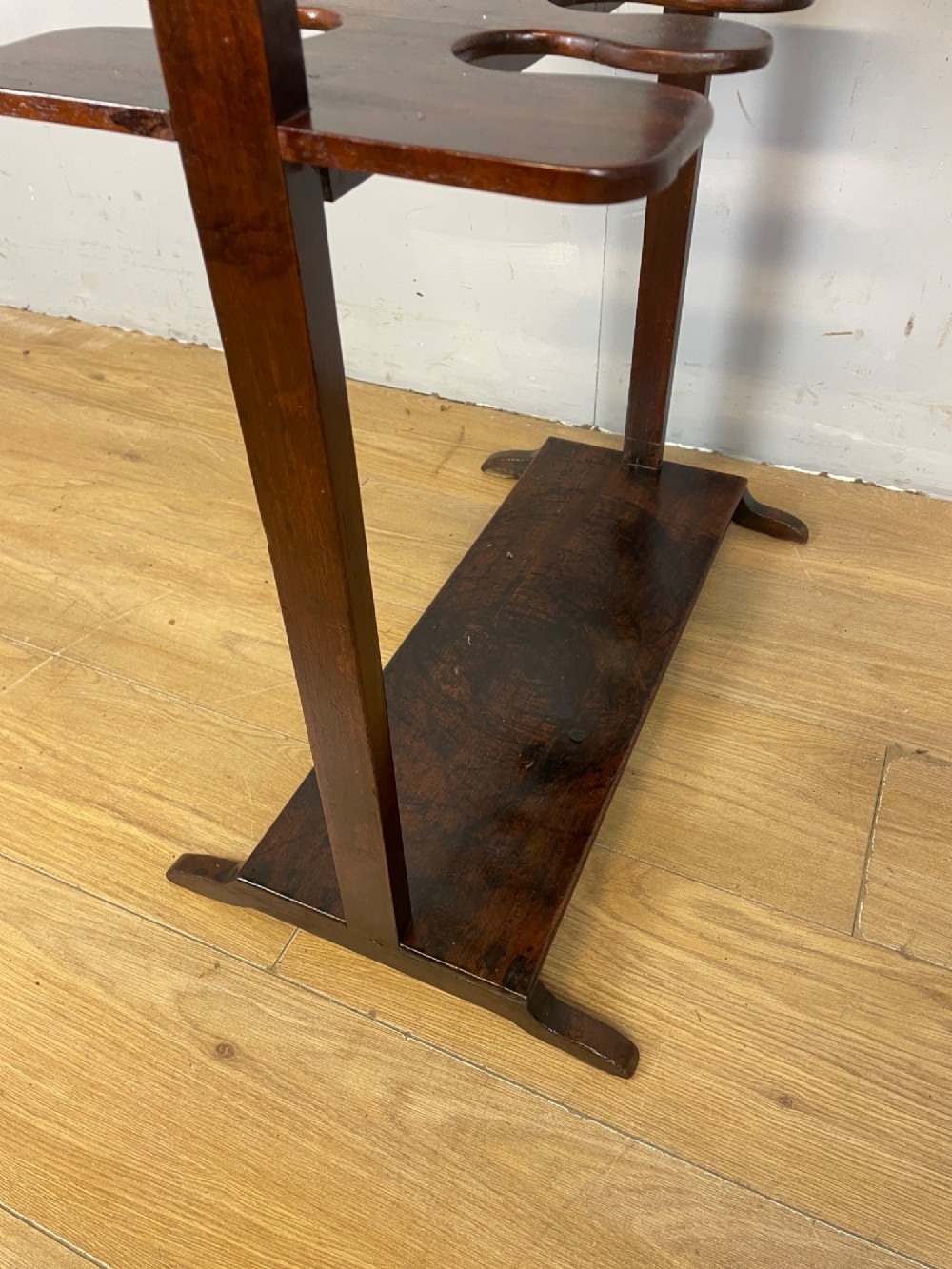 A dark mahogany Georgian boot and whip rack featuring an upper row of turned pegs, a brass handle, a central cutout shelf, and a solid base. View VII