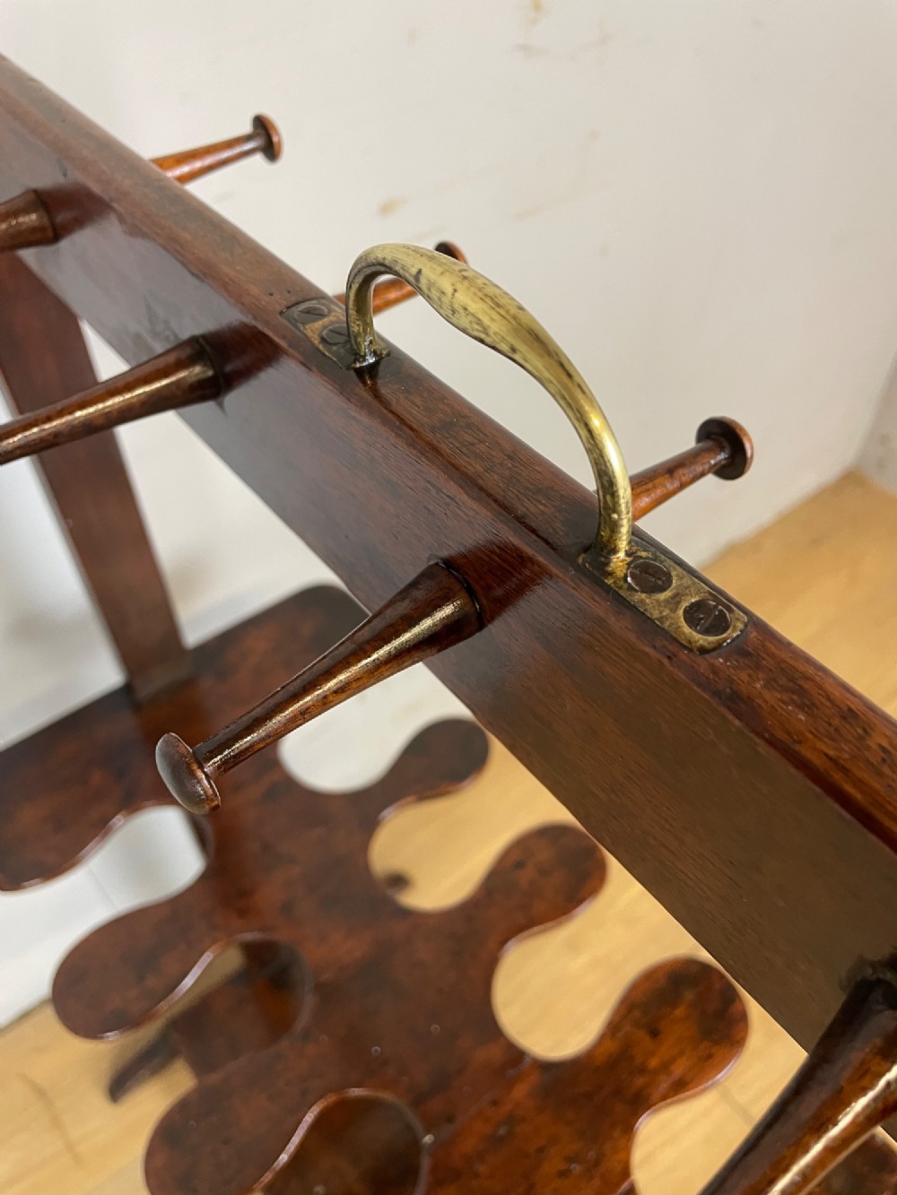 A dark mahogany Georgian boot and whip rack featuring an upper row of turned pegs, a brass handle, a central cutout shelf, and a solid base. View VIII